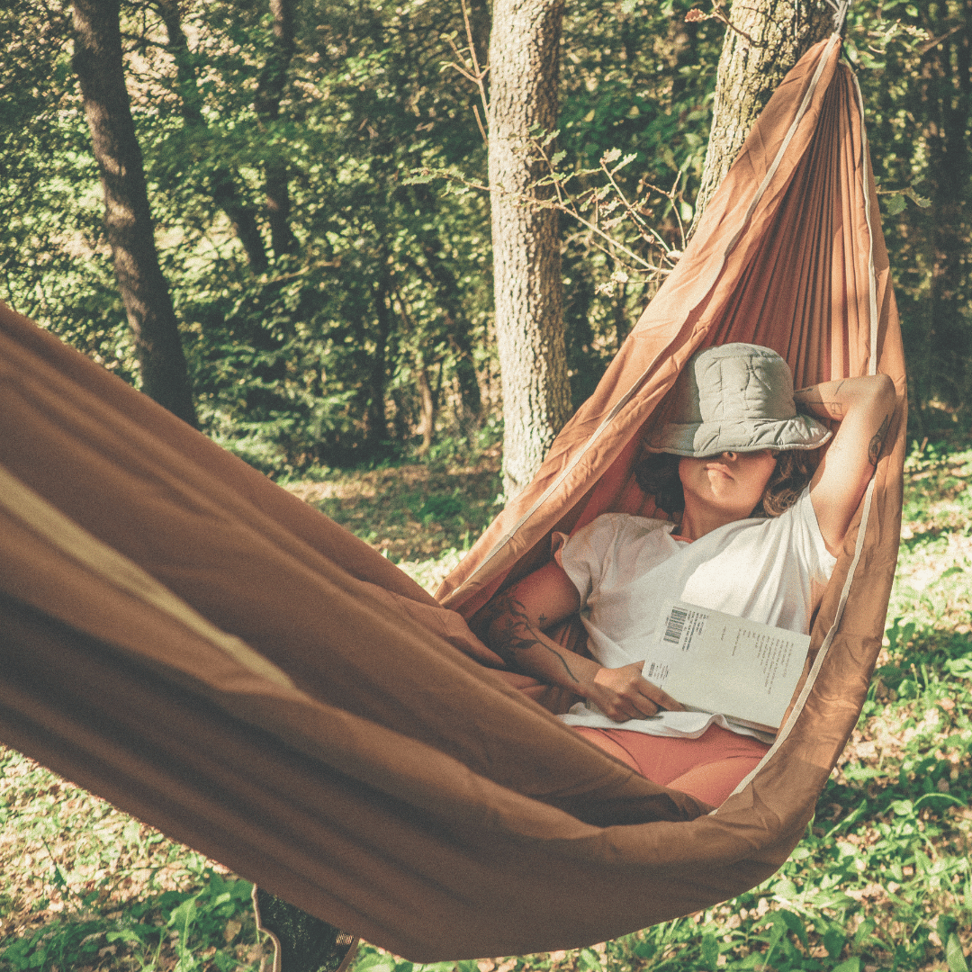 Woman sleeping with a book on her lap in a hammock in the forest.
